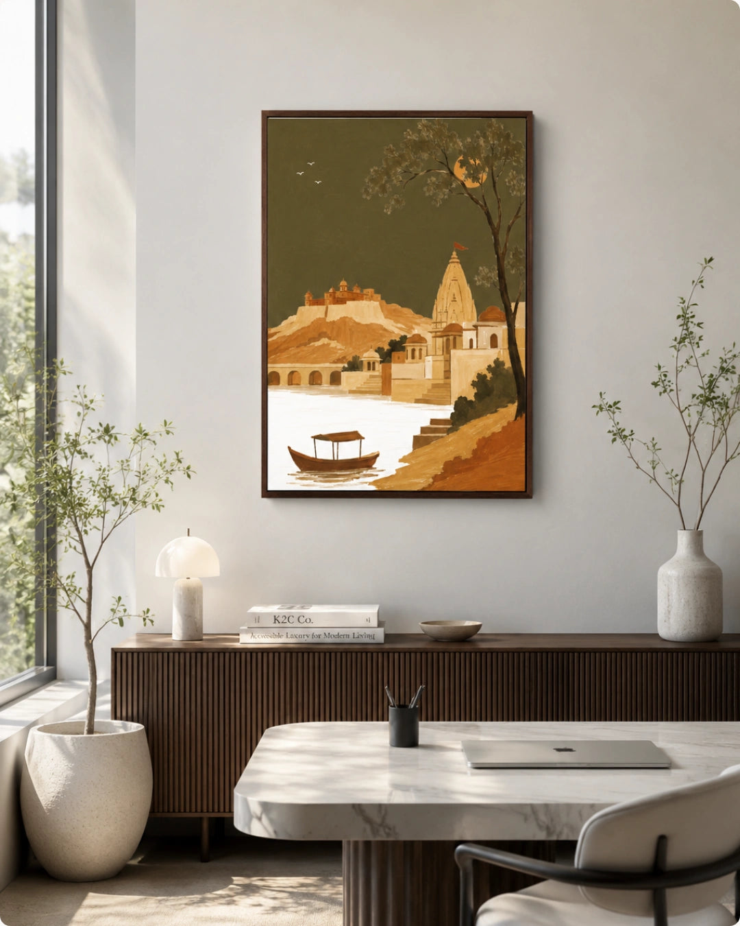 A framed art print depicting a scenic landscape with a boat on water, a church spire, and trees, displayed on a light gray wall in a modern, sunlit room with a marble table, plants, and a wooden cabinet.