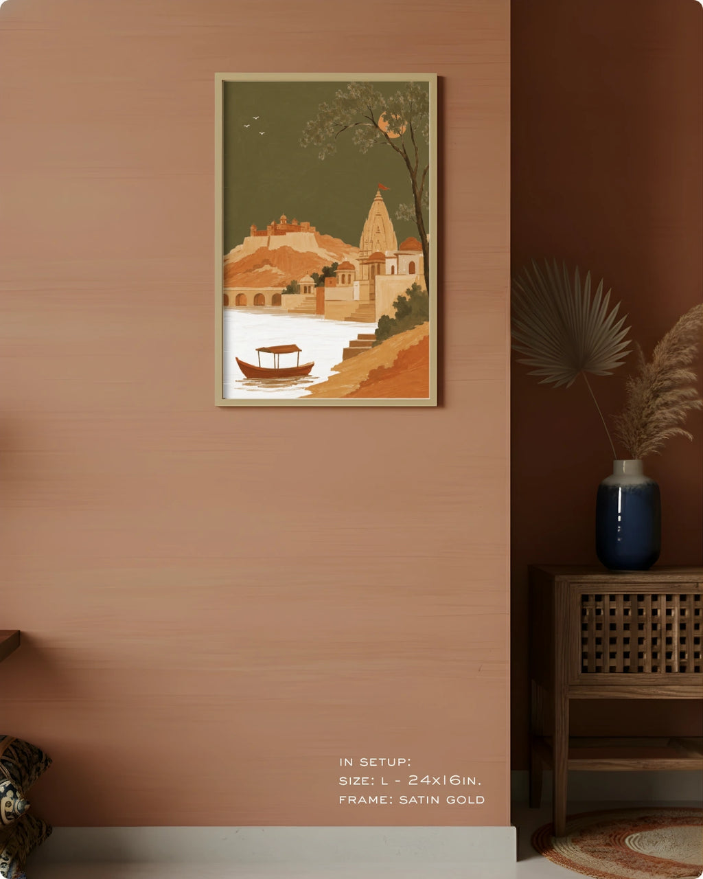 A framed art print depicting a scenic Indian coastal town with a boat on the water, displayed on a warm terracotta-colored wall in a styled room setting.