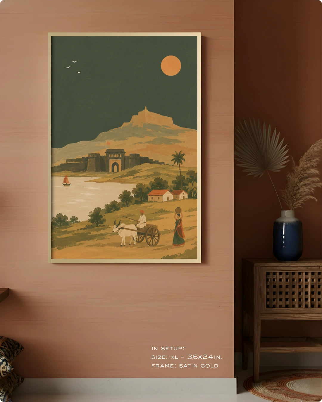 A framed vintage-style travel art print hangs on a warm terracotta wall in a styled interior. The print depicts a landscape with a castle, river, camel cart, figures, palm trees, and a large sun.