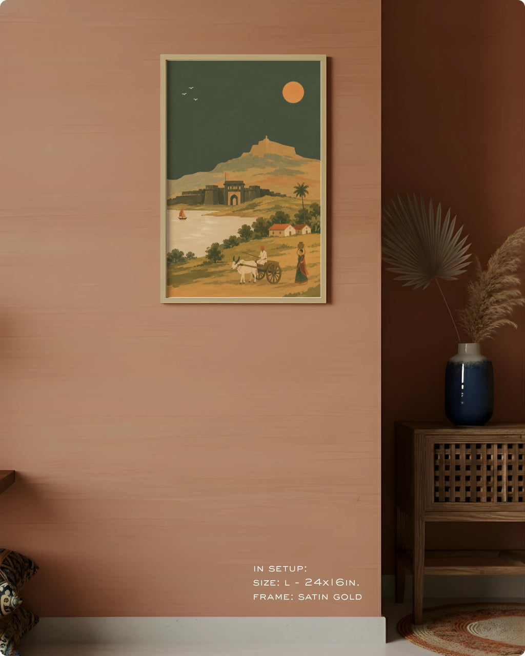 A framed art print depicting a vintage desert landscape with a camel, a woman, and a mountain under a full moon, styled on a terracotta wall next to a wooden cabinet with a blue vase.