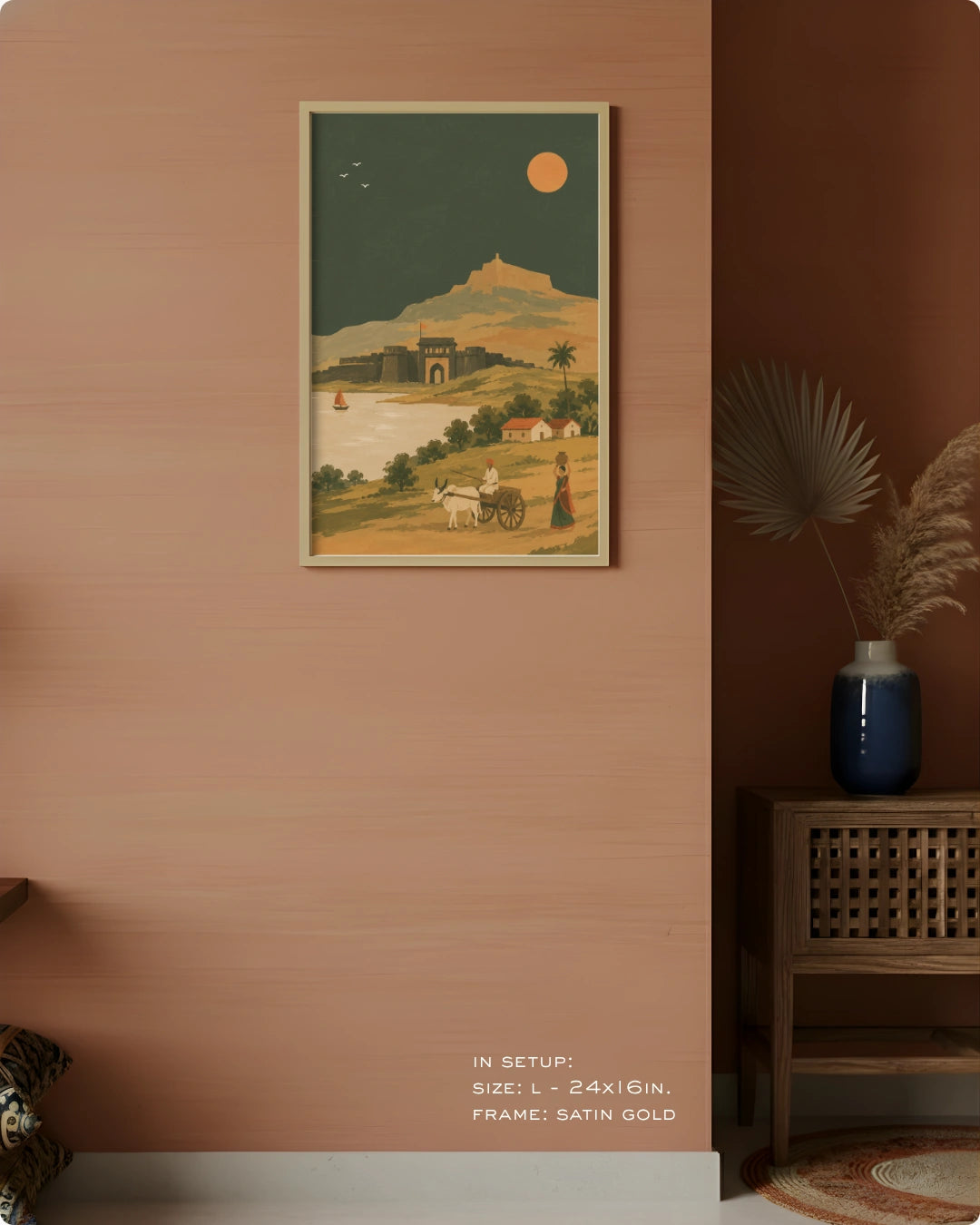 A framed art print depicting a vintage desert landscape with a camel, a woman, and a mountain under a full moon, styled on a terracotta wall next to a wooden cabinet with a blue vase.