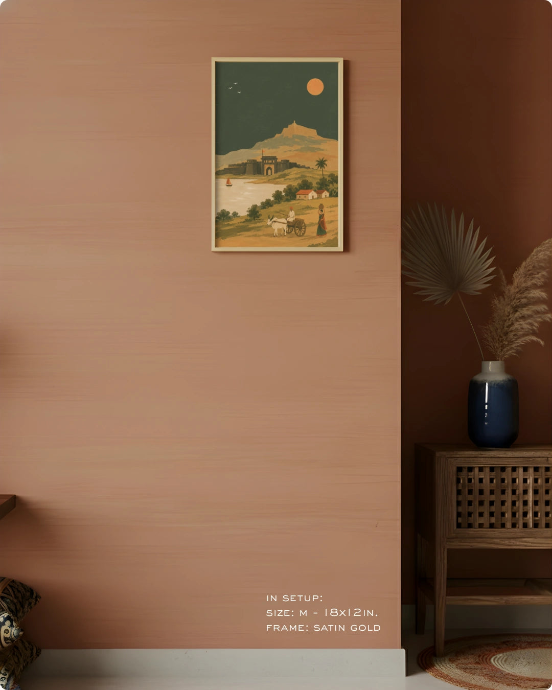 A framed art print featuring a retro-style landscape with a mountain, river, and camel under a full moon, displayed on a terracotta-colored wall in a styled interior setting.