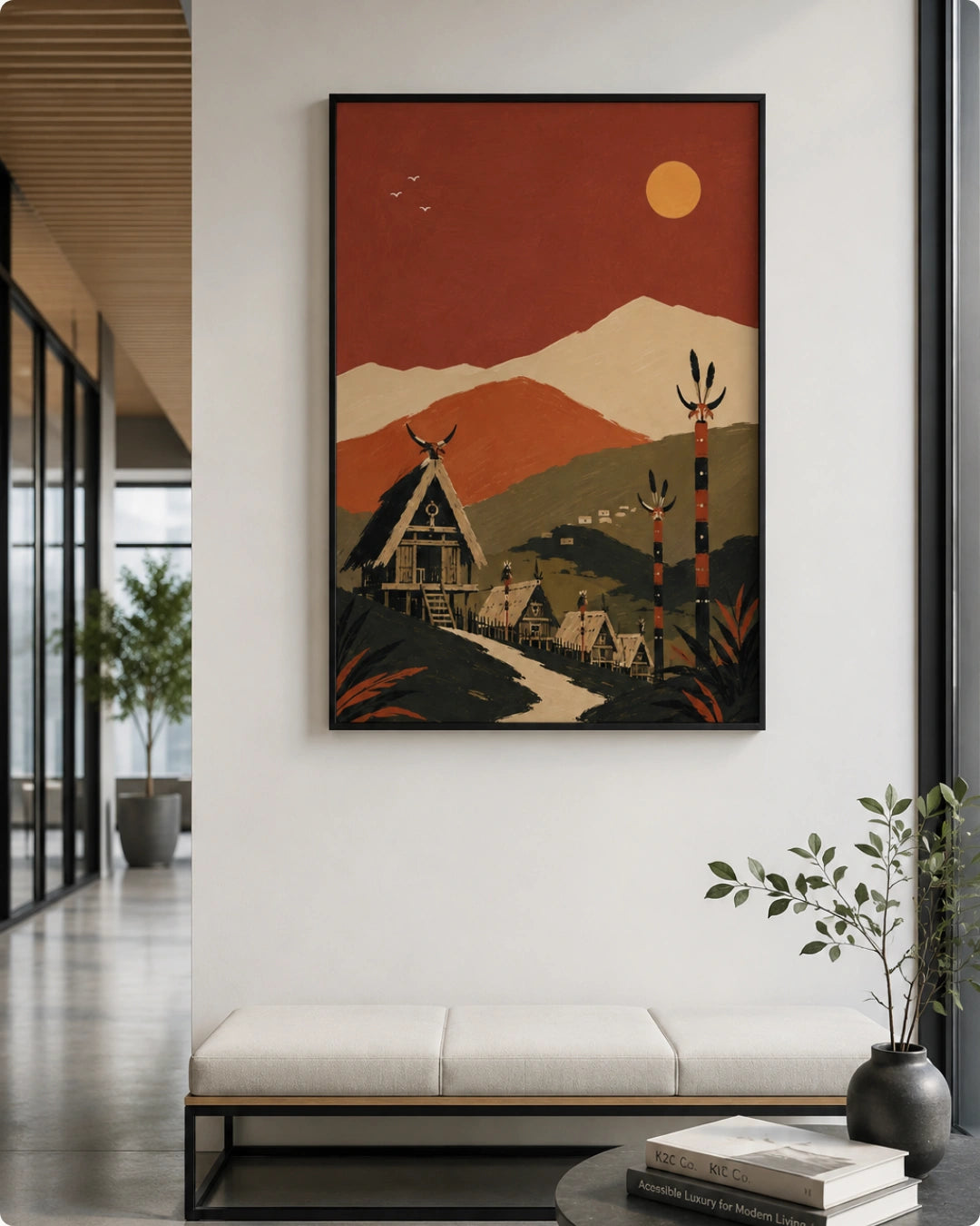 A framed art print featuring a stylized Native American-inspired village scene with A-frame houses, mountains, and a sun in warm earthy tones, displayed on a white wall in a modern interior setting.