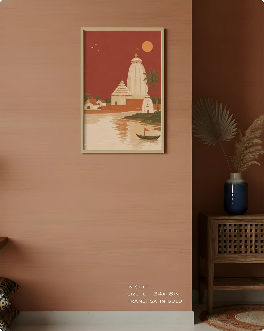 A framed art print depicting a traditional South Asian temple scene with a river, boat, and palm tree, styled on a terracotta-colored wall in a modern interior setting.