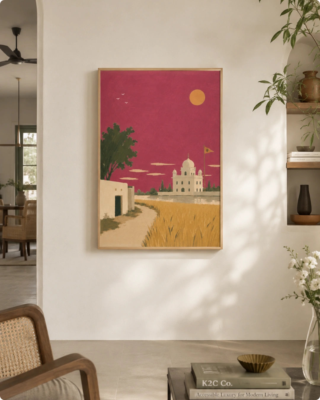 A framed art print depicting a stylized landscape with a pink sky, golden field, and white domed building, displayed on a white wall in a modern living space.