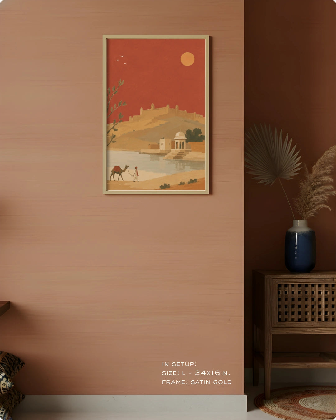 A framed art print depicting a desert landscape with a camel, domed temple, and sun, hung on a peach-colored wall in a styled interior setting.
