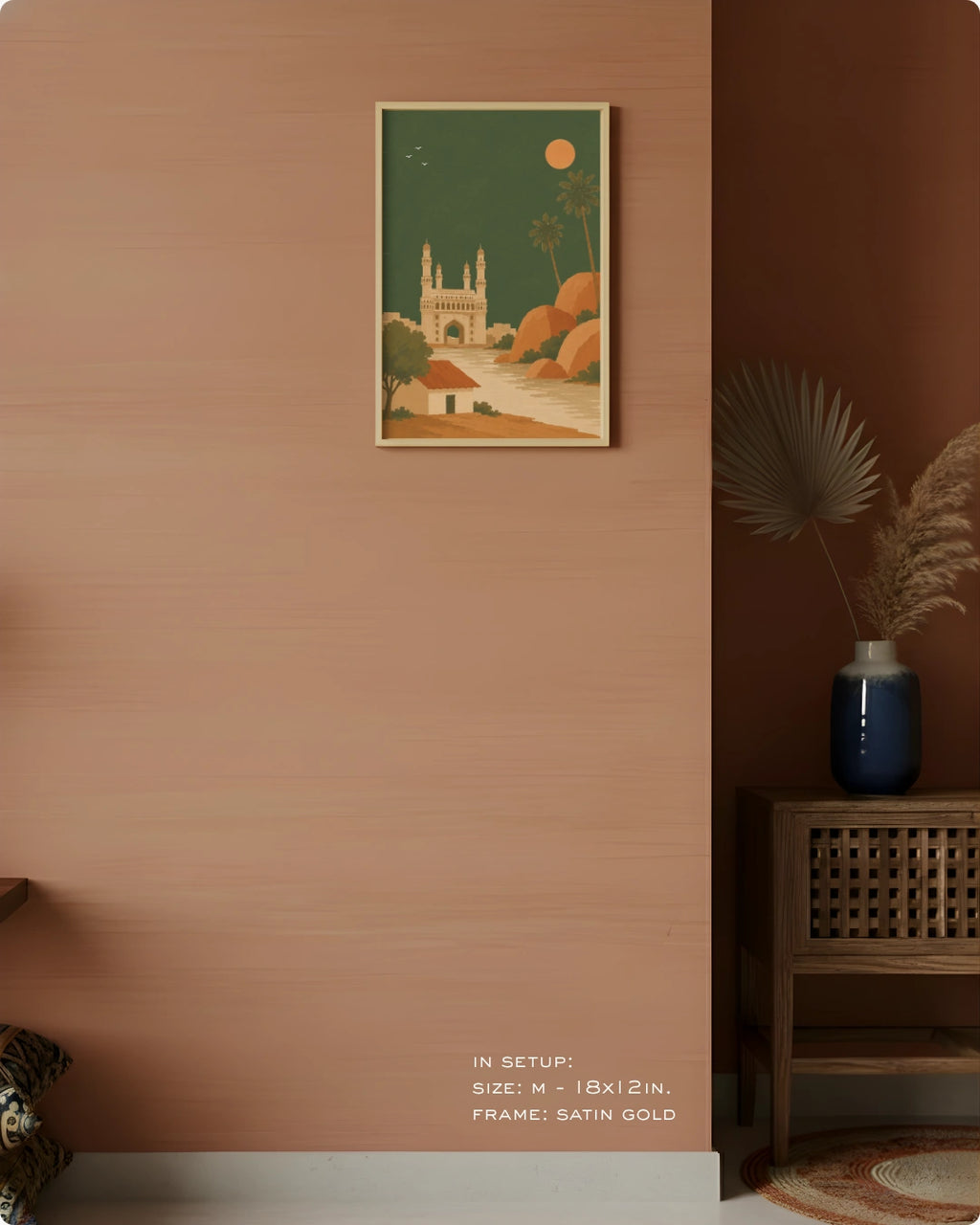 A framed art print featuring a stylized illustration of a mosque under a green sky with a sun, displayed on a terracotta-colored wall in a styled interior setting.