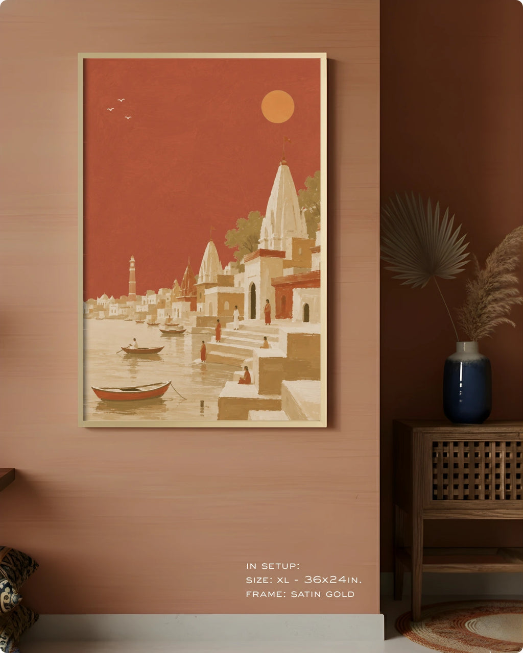 A framed art print depicting a stylized Indian coastal town with temples, boats, and a sun in a terracotta and beige palette, displayed on a warm terracotta wall in a styled interior setting.