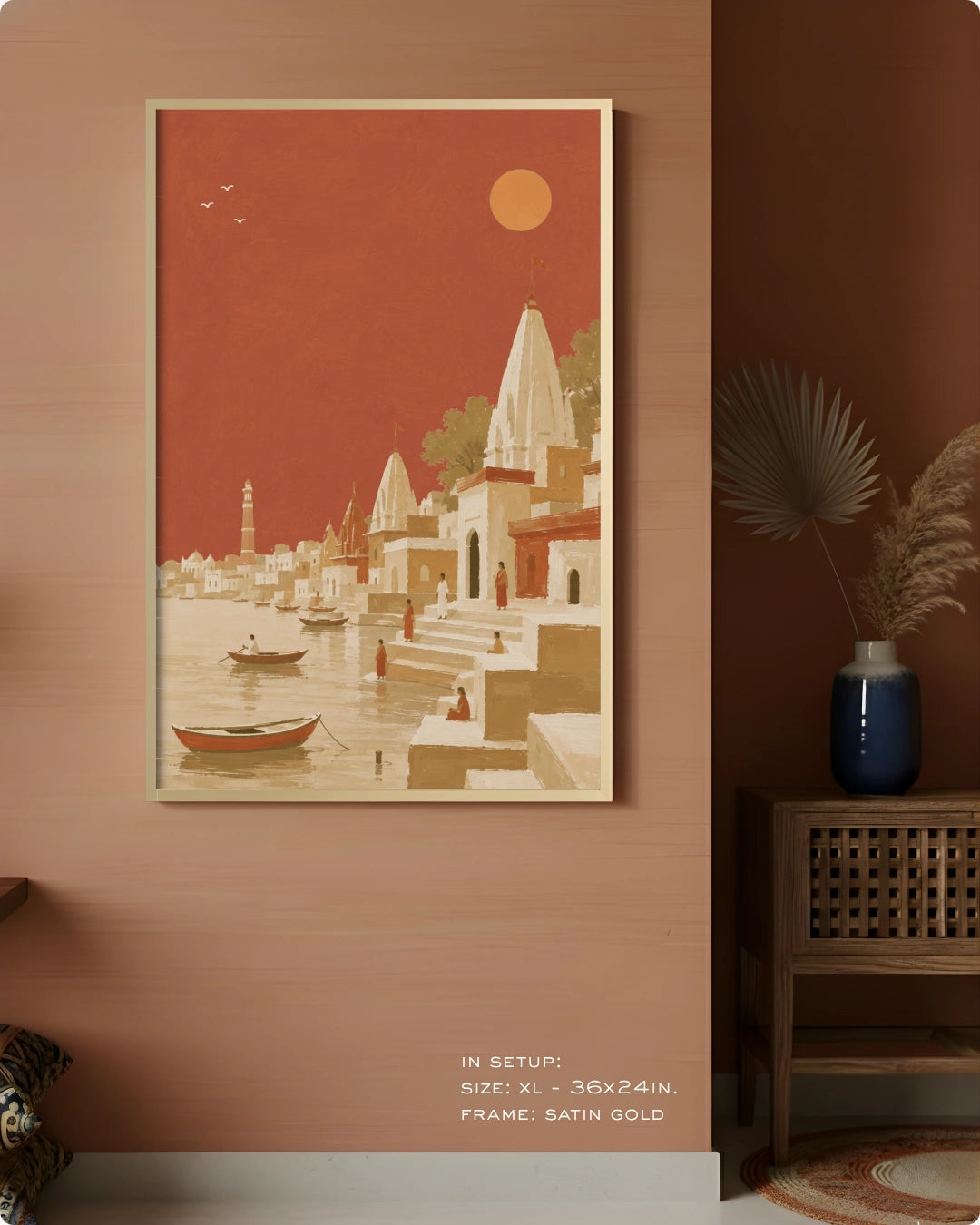 A framed art print depicting a stylized Indian coastal town with temples, boats, and a sun in a terracotta and beige palette, displayed on a warm terracotta wall in a styled interior setting.