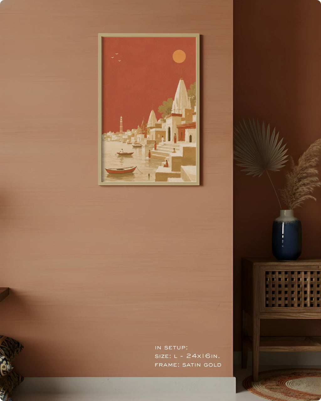 A framed art print depicting a stylized Indian Gurgaon landscape with temples, boats, and a red sky, mounted on a textured terracotta wall in a styled interior setting.