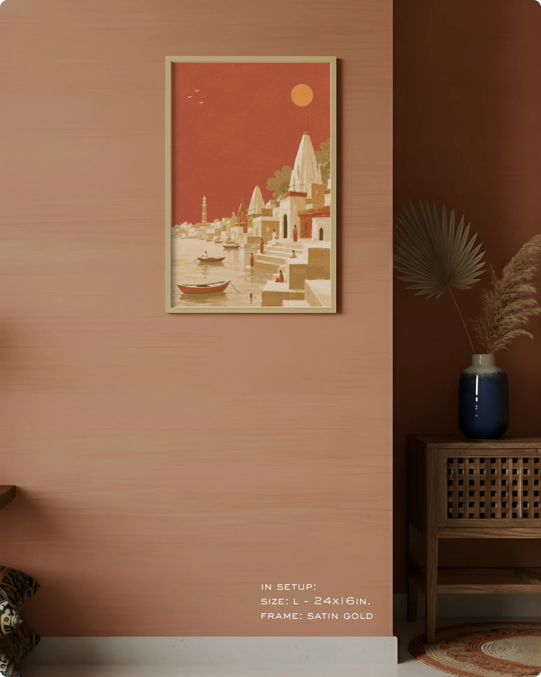 A framed art print depicting a stylized Indian Gurgaon landscape with temples, boats, and a red sky, mounted on a textured terracotta wall in a styled interior setting.