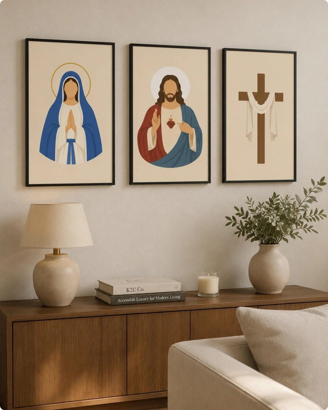 Three framed religious art prints hang on a beige wall above a wooden console table in a styled living room. The prints show a stylized depiction of the Virgin Mary in blue and white, Jesus Christ with red and blue robes, and a brown Christian cross.