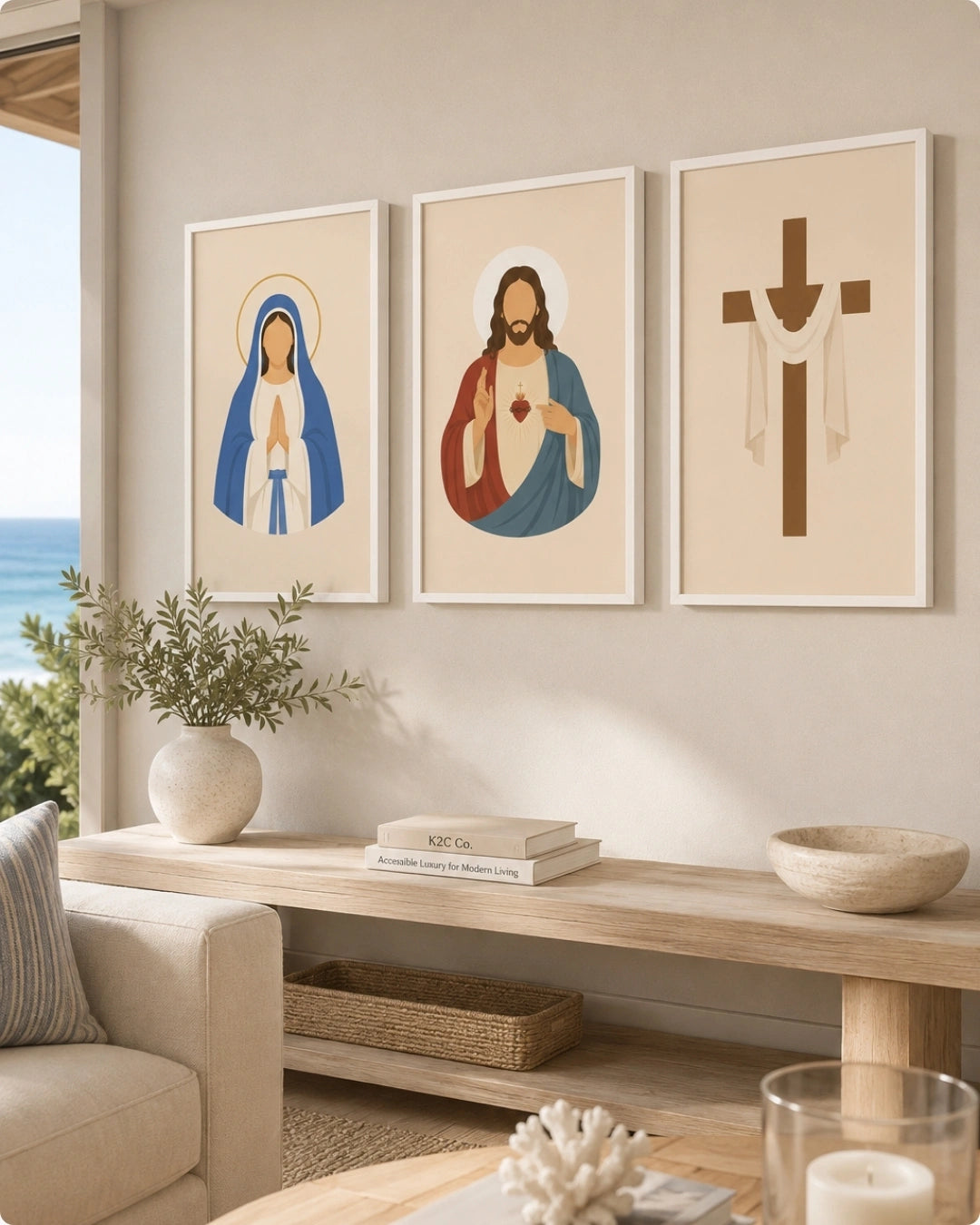 Three framed wall art prints with religious illustrations hang above a light wood console table in a styled living room. The left print shows a robed figure in blue and white with a halo, the center print shows a bearded figure in red and blue with a heart, and the right print shows a brown cross with white drapery.