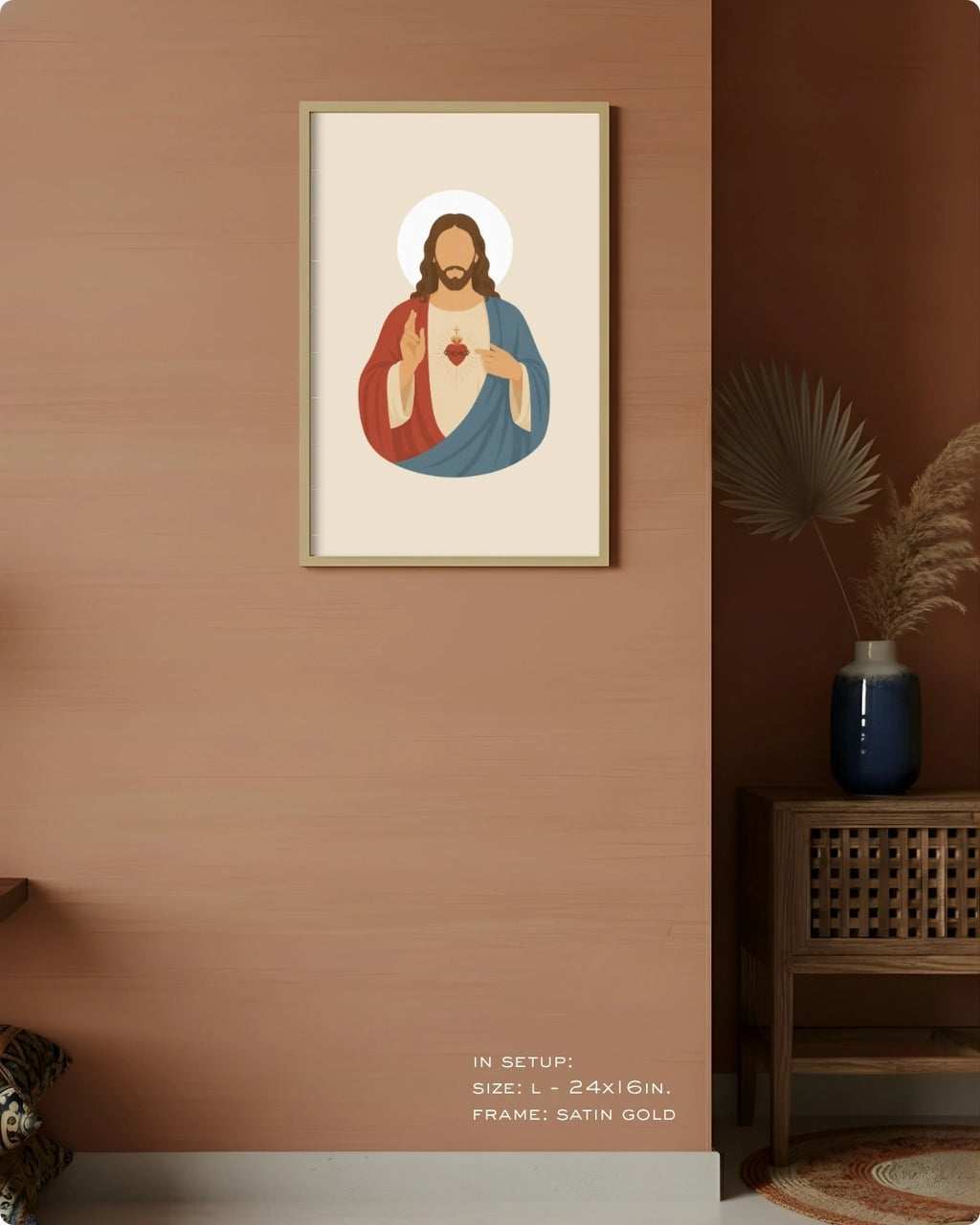 A framed art print of Jesus Christ with a gold frame, displayed on a warm terracotta wall in a styled room setting with a wooden side table and a blue vase.