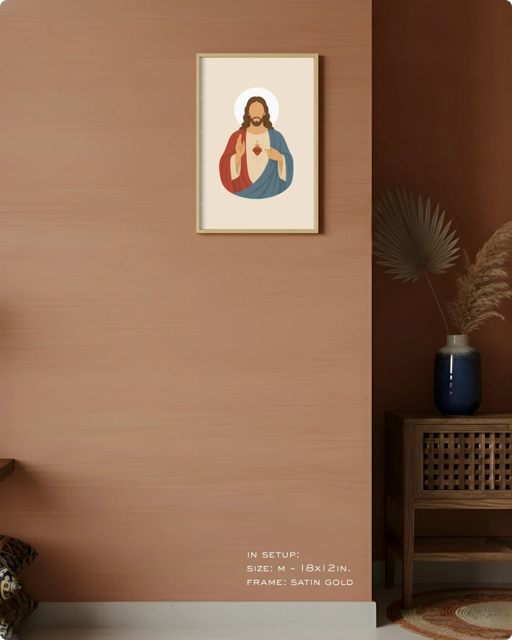 A framed art print featuring a stylized religious icon of Jesus Christ with a gold frame, displayed on a textured terracotta wall in a styled interior setting with a wooden side table and vase.