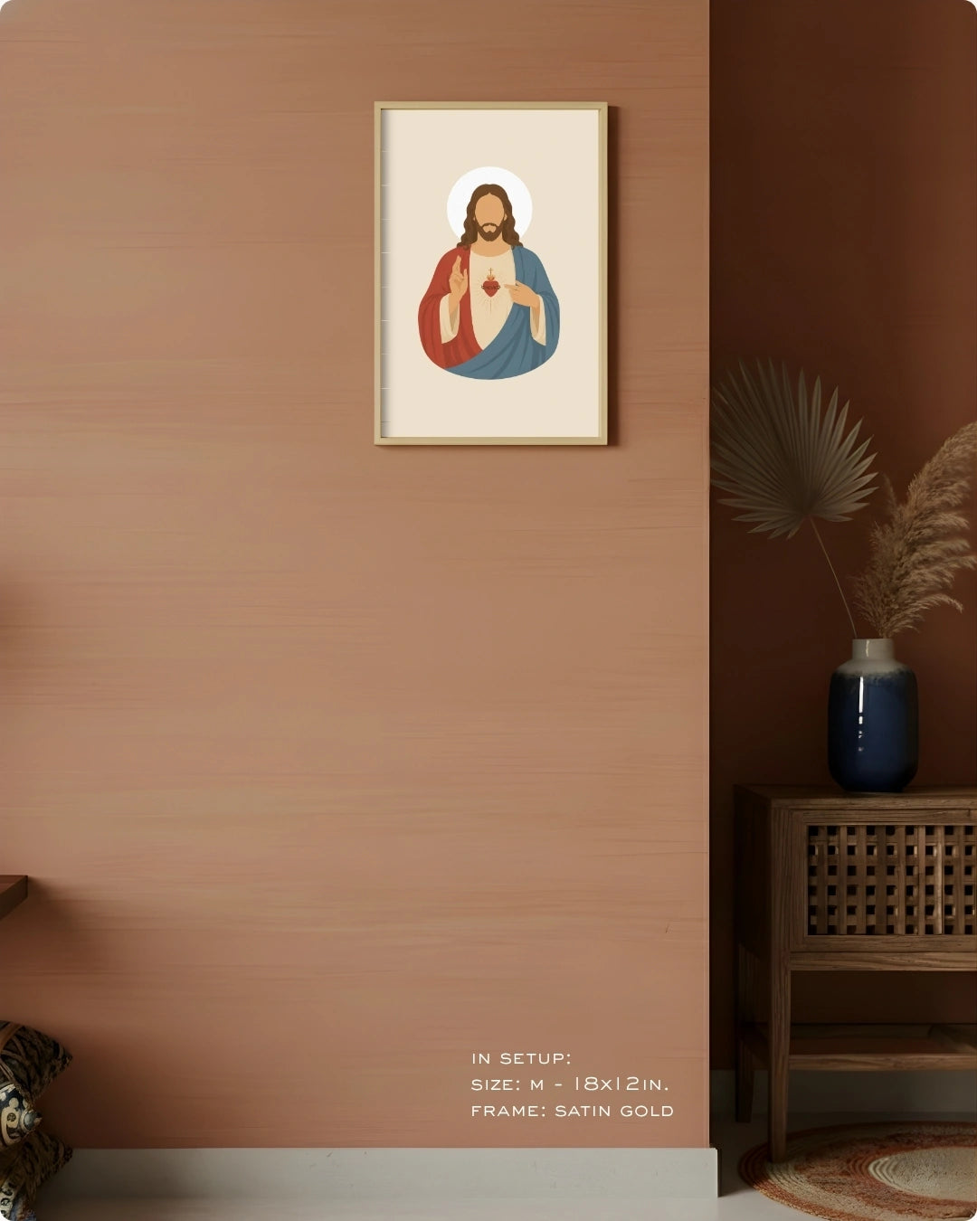 A framed art print featuring a stylized religious icon of Jesus Christ with a gold frame, displayed on a textured terracotta wall in a styled interior setting with a wooden side table and vase.