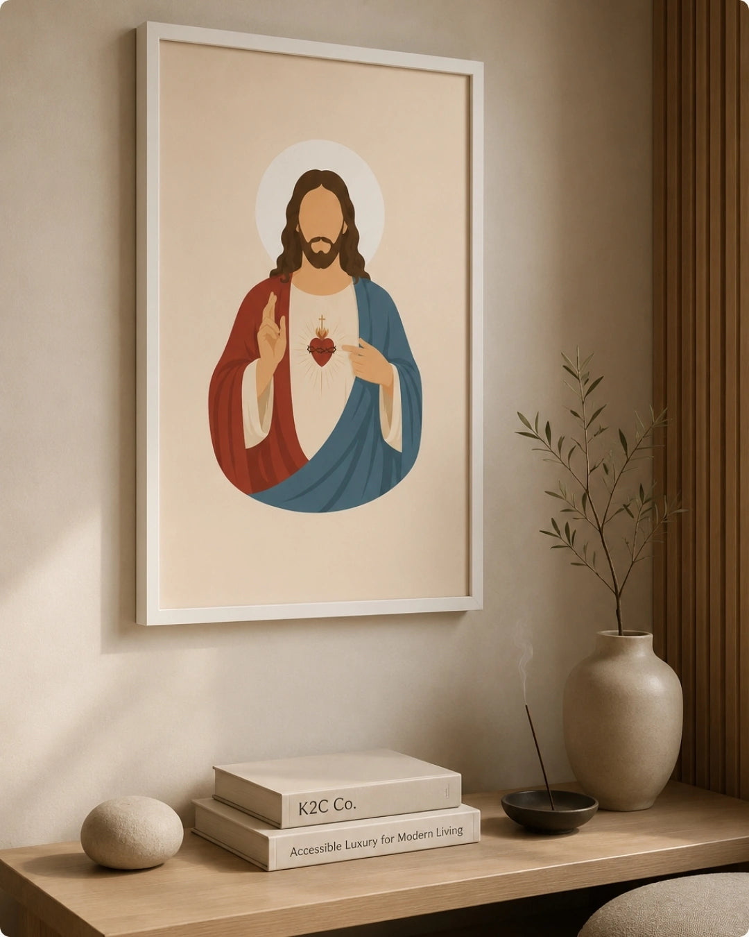 A framed art print of the Sacred Heart of Jesus hangs on a beige wall above a wooden console table styled with books, a vase, and a plant.