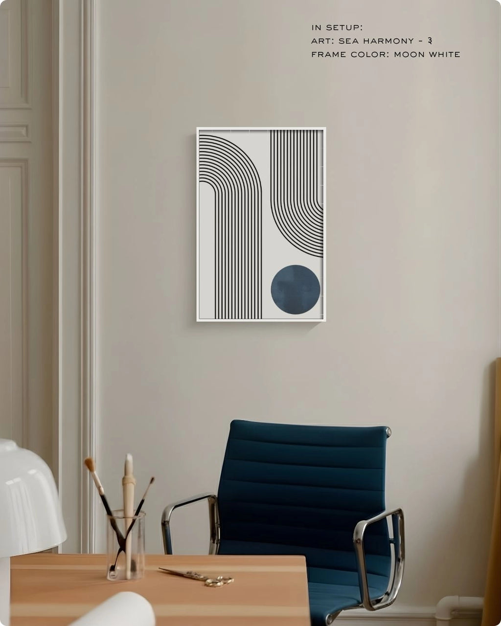 Sea Harmony 3 abstract wall art by K2C Co. featuring a deep blue circle and black curved lines in a Moon White frame, displayed in a minimalist office setting with a blue desk chair.
