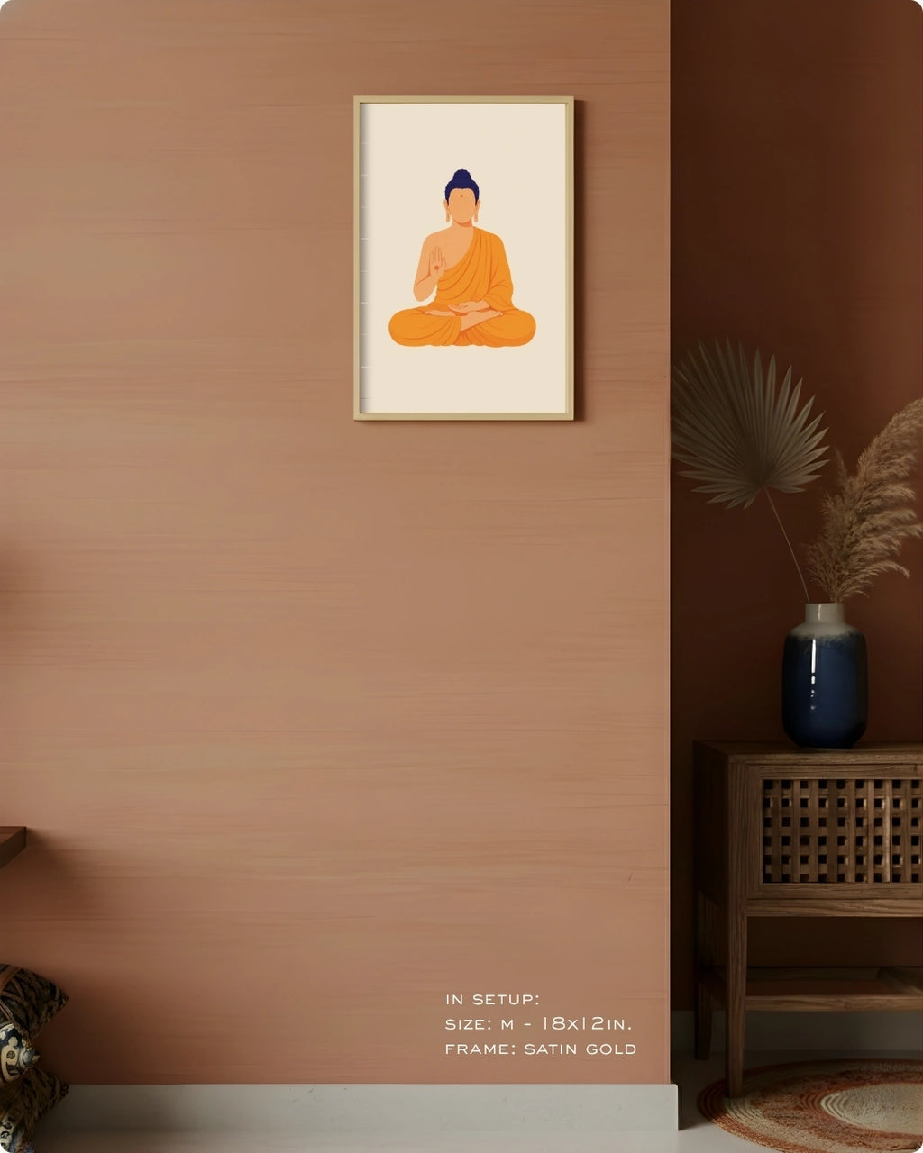 A framed minimalist art print of a meditating Buddha in orange and blue, displayed on a textured terracotta wall in a styled interior setting with a wooden side table and a blue vase.