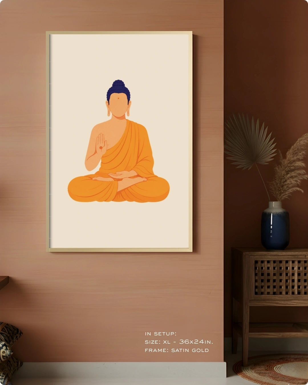 A framed minimalist art print of a seated Buddha in orange robes with a blue head, displayed on a warm brown wall in a styled interior setting with a side table and vase.