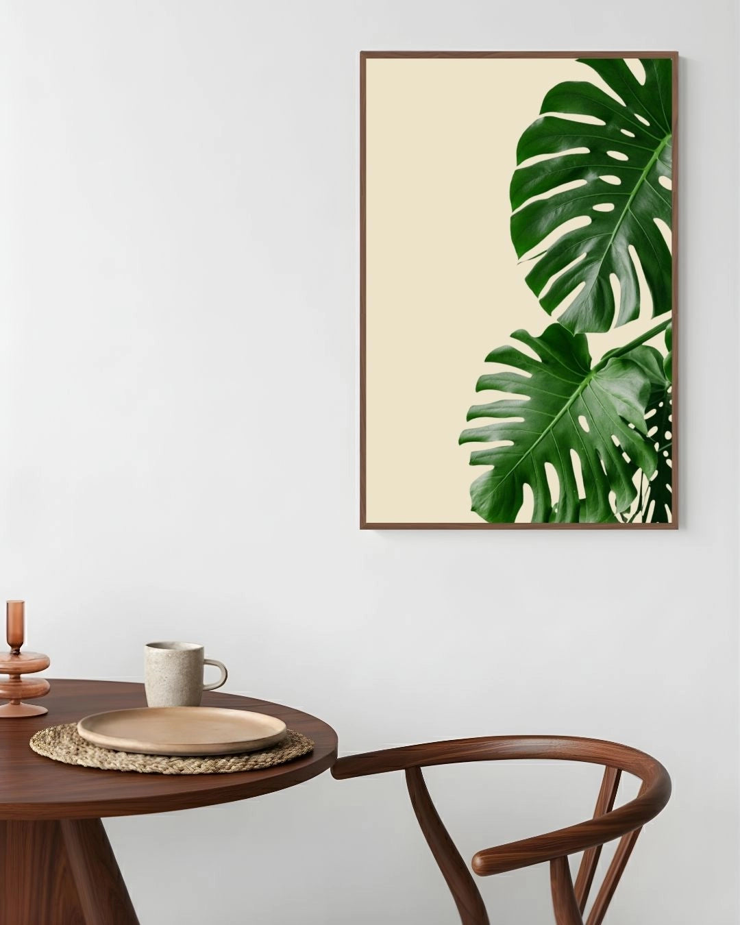 Framed artwork of green leaves on a wall above a wooden table with decor items.