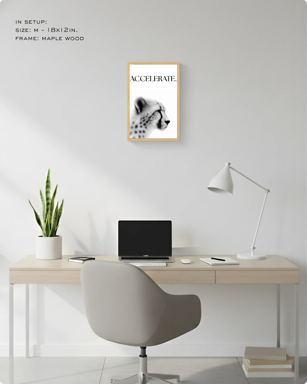 A framed wall art print featuring a black-and-white cheetah portrait with the word 'ACCELERATE' in a light wood frame, displayed above a minimalist desk setup in a bright home office.