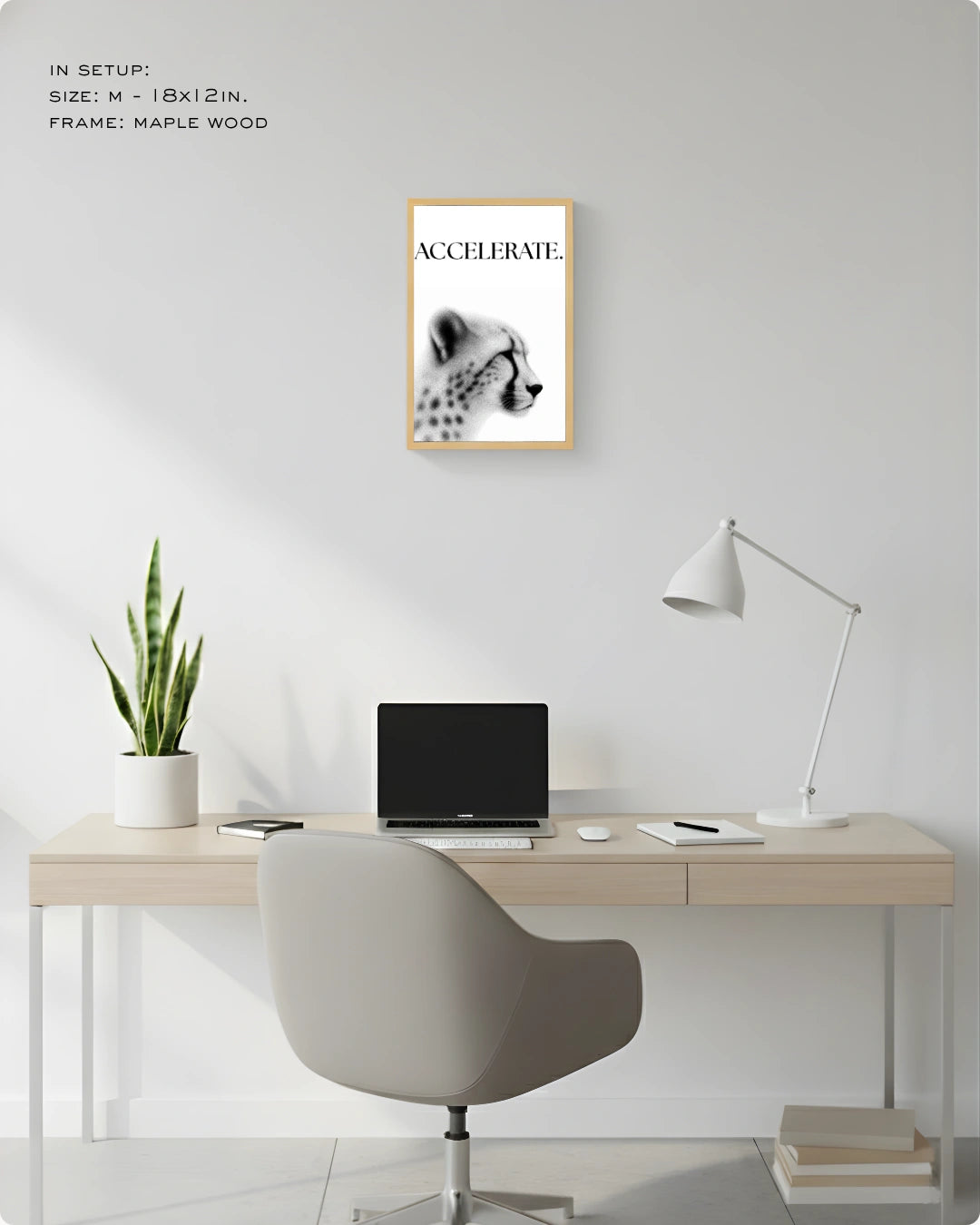 A framed wall art print featuring a black-and-white cheetah portrait with the word 'ACCELERATE' in a light wood frame, displayed above a minimalist desk setup in a bright home office.