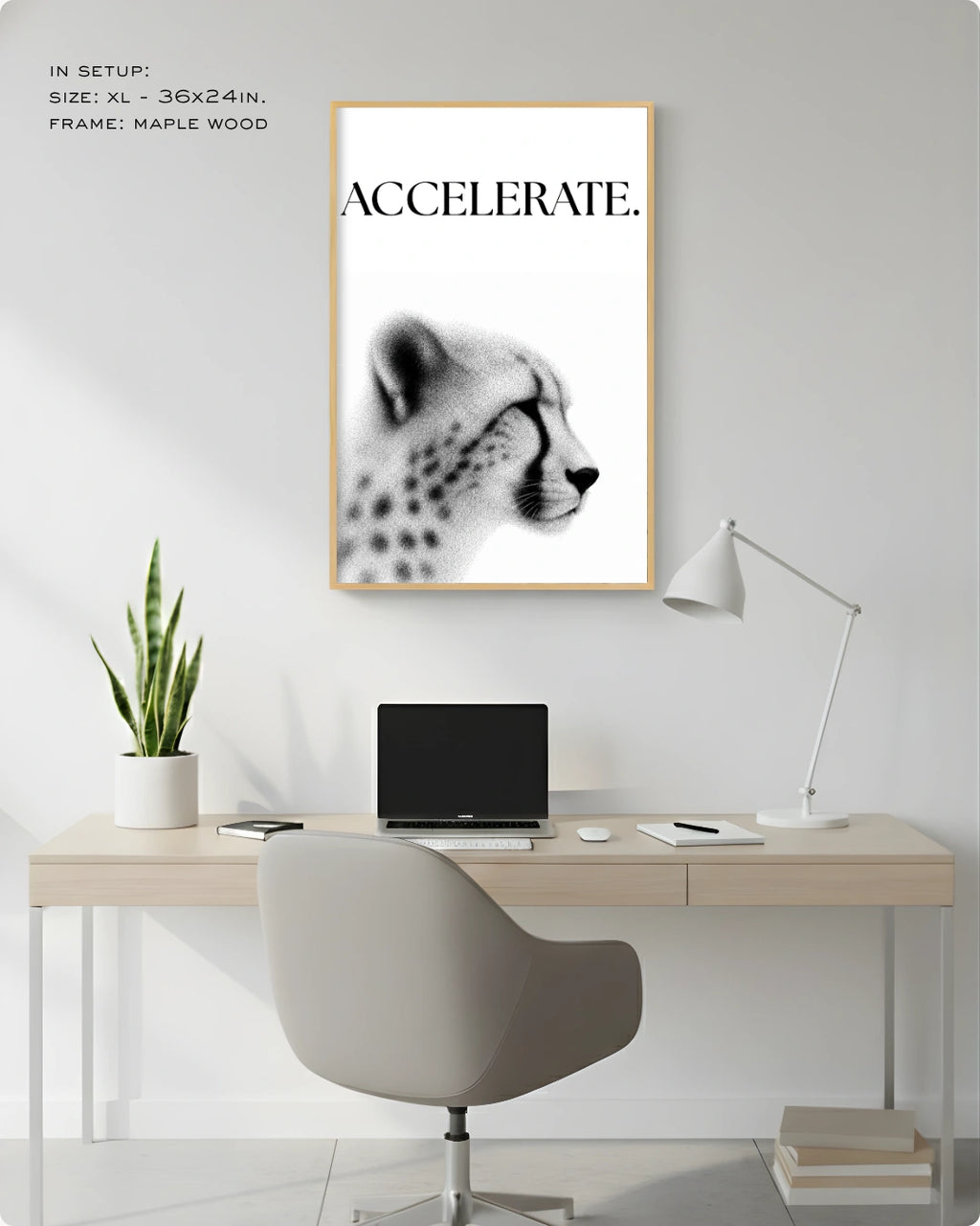 A framed black and white art print featuring a cheetah profile with the word 'ACCELERATE.' at the top, displayed on a light gray wall above a minimalist desk setup with a chair, laptop, lamp, and plant.
