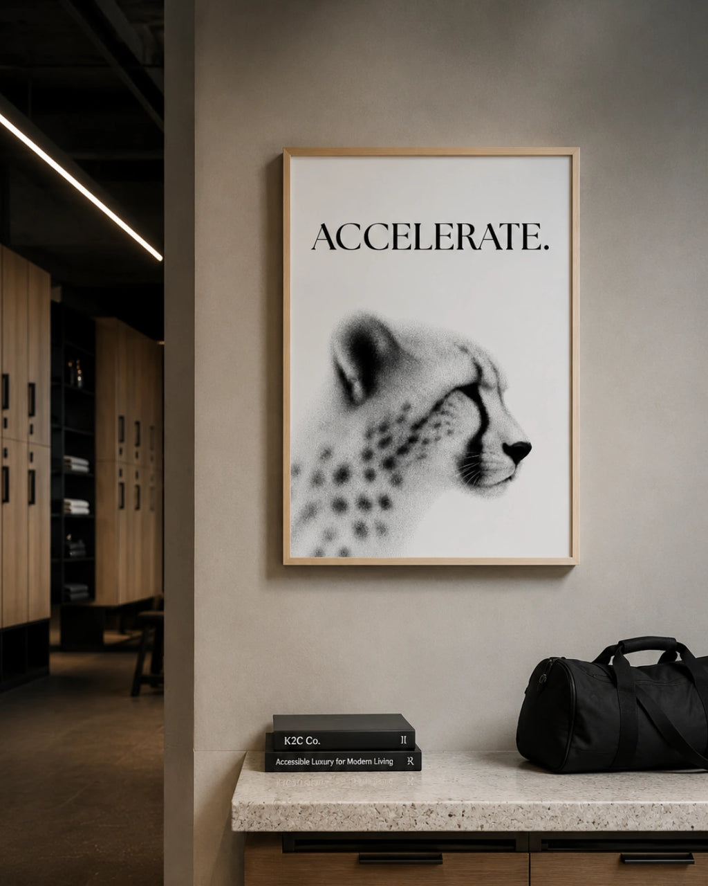 A framed black and white art print featuring a cheetah profile and the word 'ACCELERATE.' in bold text, hanging on a beige wall above a stone counter with books and a black duffel bag in a modern interior setting.