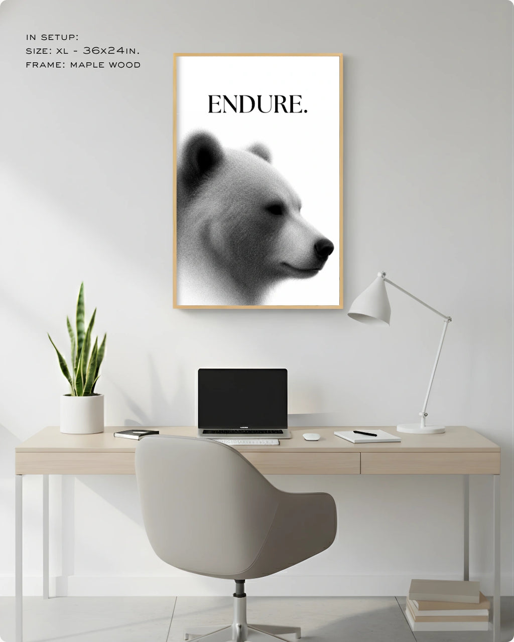 A framed black and white art print featuring a bear profile with the word 'ENDURE.' at the top, displayed on a light gray wall above a minimalist desk setup with a chair, laptop, lamp, and plant.