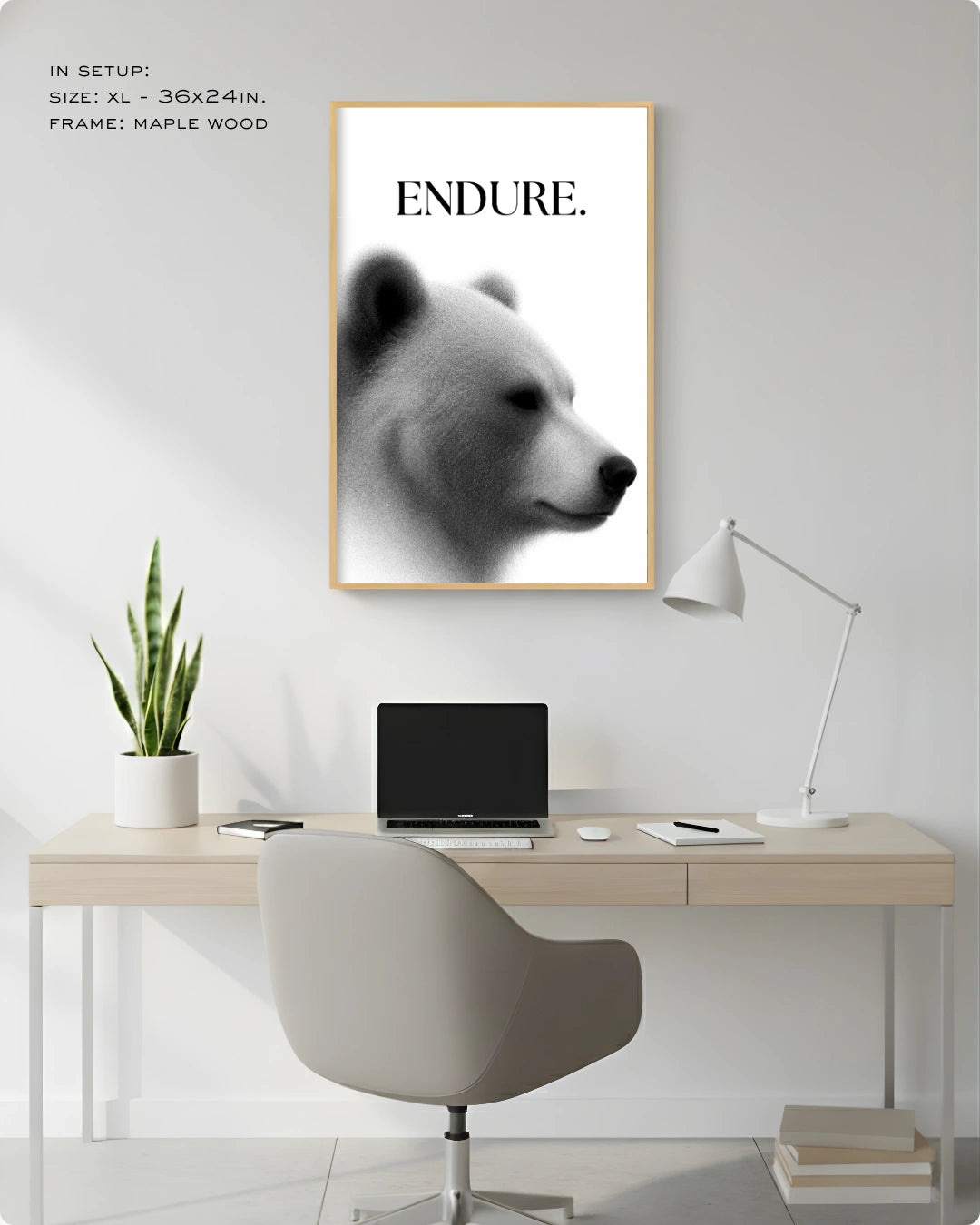A framed black and white art print featuring a bear profile with the word 'ENDURE.' at the top, displayed on a light gray wall above a minimalist desk setup with a chair, laptop, lamp, and plant.