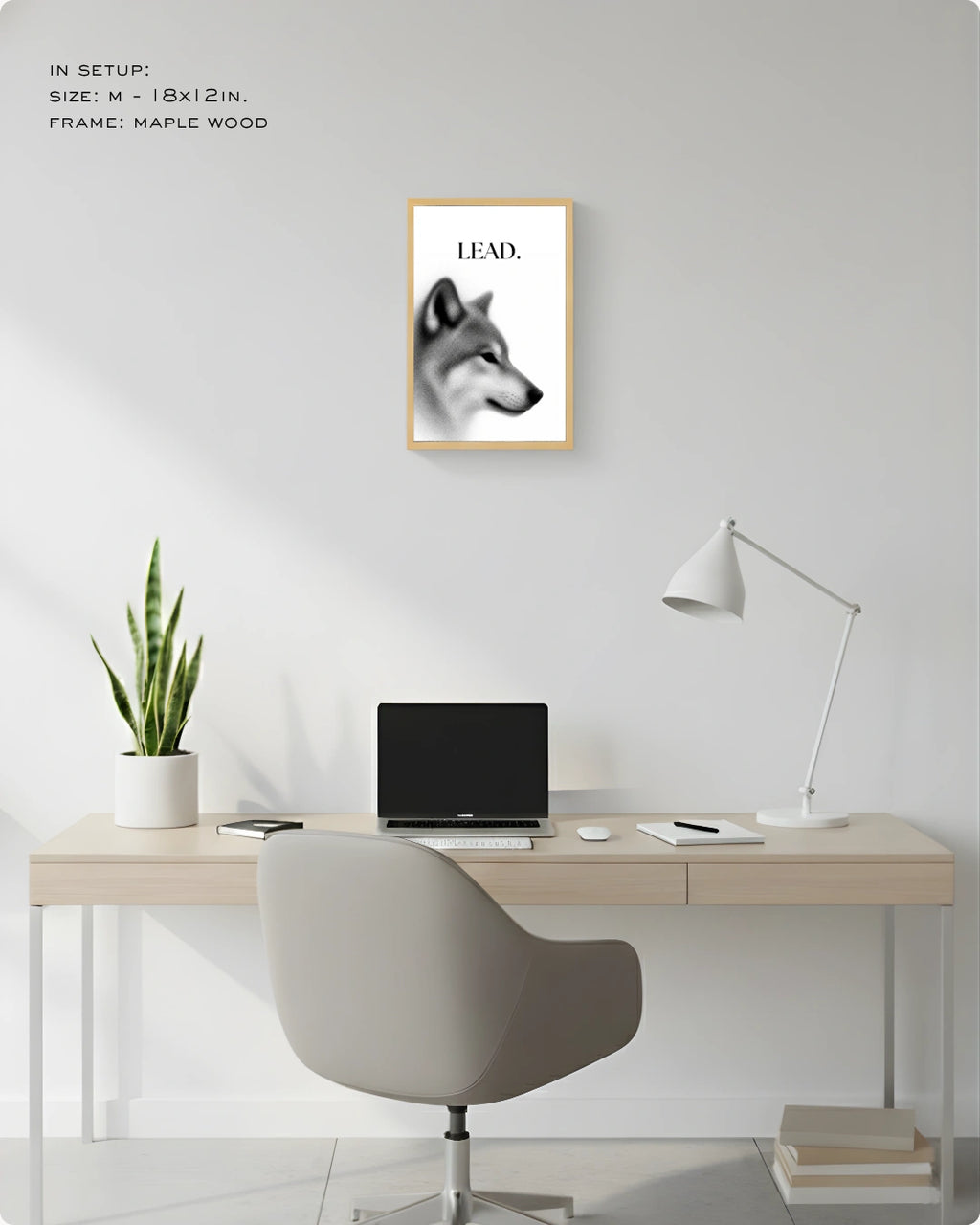 A framed black and white wolf art print with the word 'LEAD.' hanging on a light gray wall above a minimalist desk setup with a laptop, lamp, chair, and plant.