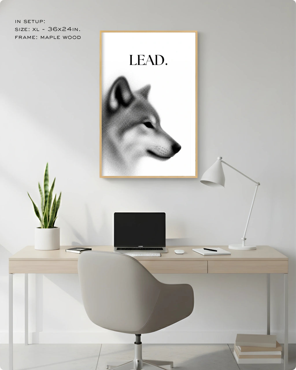 A framed wall art print featuring a black-and-white wolf head with the word 'LEAD.' above it, shown hanging above a desk in a modern home office setup.